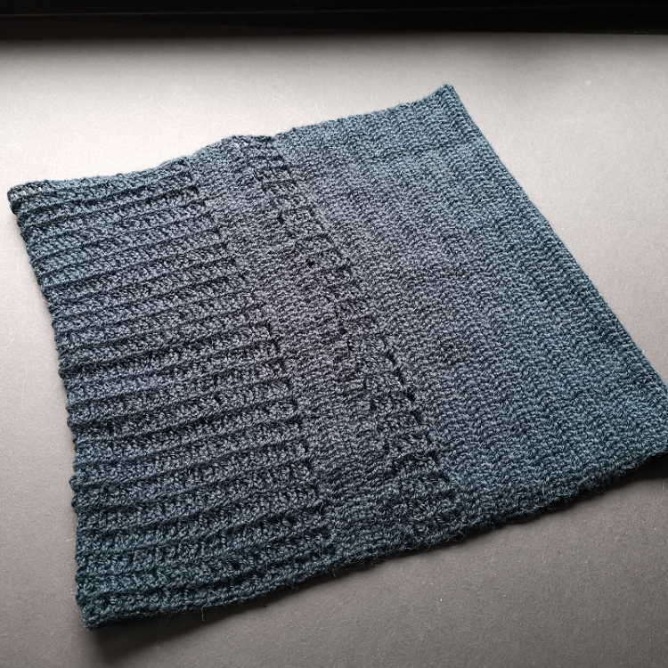 Grey background with a very dark petrol/teal alpaca cowl.  Stitch definition shows the two different stitches used throughout the cowl.