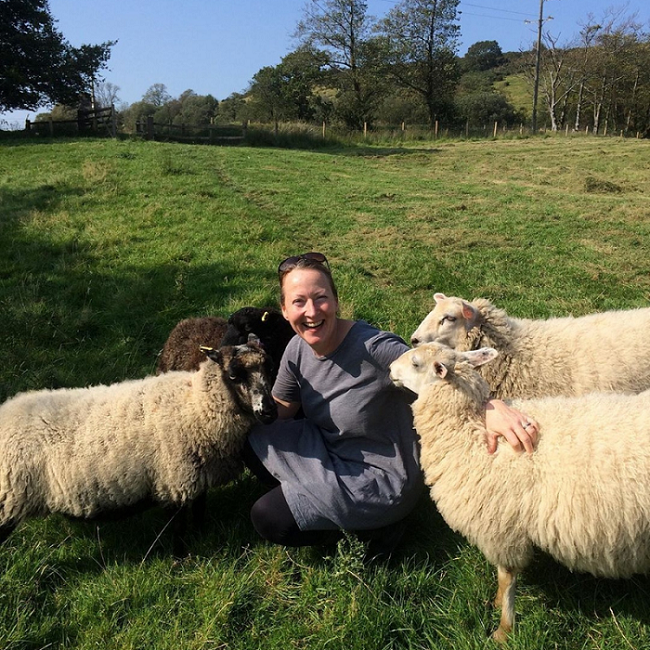 Photo of Helen crouching in a field, cuddling sheep.